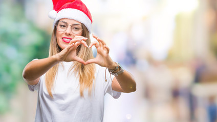 Obraz premium Young beautiful woman wearing christmas hat over isolated background smiling in love showing heart symbol and shape with hands. Romantic concept.