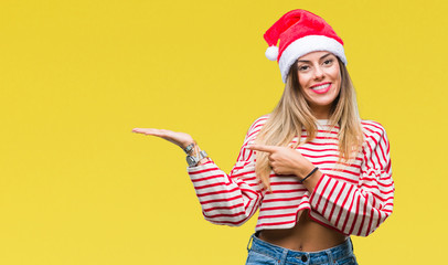 Obraz premium Young beautiful woman wearing christmas hat over isolated background amazed and smiling to the camera while presenting with hand and pointing with finger.