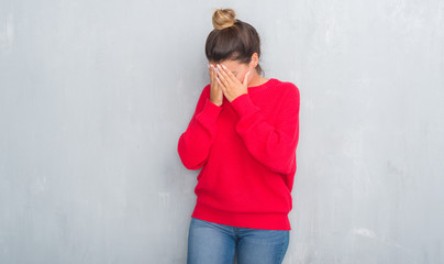 Young adult woman over grey grunge wall wearing winter outfit with sad expression covering face with hands while crying. Depression concept.