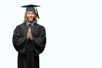 Young handsome graduated man with long hair over isolated background praying with hands together asking for forgiveness smiling confident.