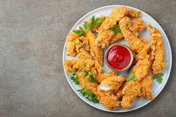 Breaded chicken strips with tomato ketchup on a white plate. Fast food on dark brown background....