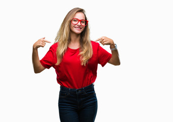 Obraz na płótnie Canvas Young beautiful blonde woman wearing glasses over isolated background looking confident with smile on face, pointing oneself with fingers proud and happy.