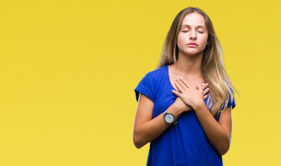 Obraz premium Young beautiful blonde woman over isolated background smiling with hands on chest with closed eyes and grateful gesture on face. Health concept.