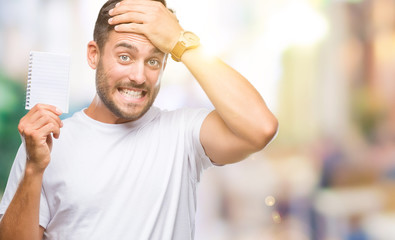 Obraz premium Young handsome man holding notebook over isolated background stressed with hand on head, shocked with shame and surprise face, angry and frustrated. Fear and upset for mistake.