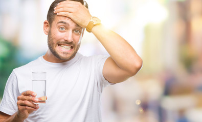 Young handsome man drinking glass of water over isolated background stressed with hand on head, shocked with shame and surprise face, angry and frustrated. Fear and upset for mistake.