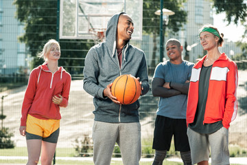 Great mood. Positive delighted man laughing with his friends while going to play basketball