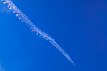 Condensation trail from airplane on blue sky clouds.