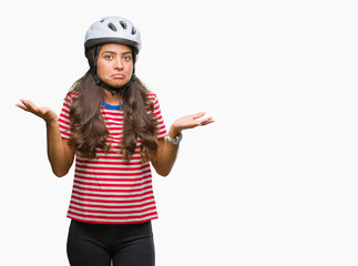 Young arab cyclist woman wearing safety helmet over isolated background clueless and confused...