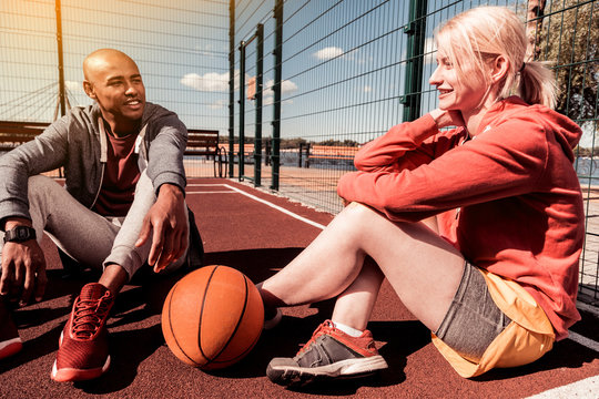 Love to basketball. Positive nice woman touching the basketball ball with her leg while talking to her boyfriend
