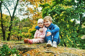 Brother and sister in autumn Park . Children on a walk on a warm autumn day . Children are dressed in warm tracksuits