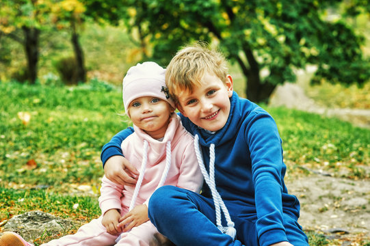 Brother and sister in autumn Park . Children on a walk on a warm autumn day . Children are dressed in warm tracksuits