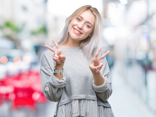 Fototapeta premium Young blonde woman over isolated background smiling looking to the camera showing fingers doing victory sign. Number two.