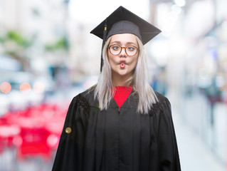 Young blonde woman wearing graduate uniform over isolated background making fish face with lips,...
