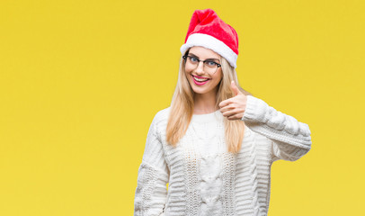 Young beautiful blonde woman wearing christmas hat over isolated background doing happy thumbs up gesture with hand. Approving expression looking at the camera with showing success.