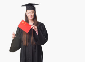 Young Chinese woman wearing graduate uniform holding China flag with a happy face standing and smiling with a confident smile showing teeth