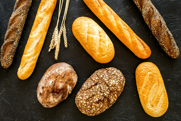 Bakery concept. Fresh white and brown bread. Loaf and baguette decorated with wheat ears on black...
