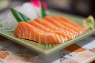 Close up of Salmon raw sashimi on green Japanese traditional dish on the table.