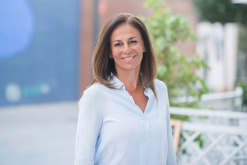 Beautiful middle age hispanic woman standing with smile on face at the street. Walking through the city while smiling confident and cheerful on a sunny day.