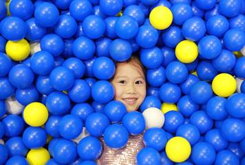 Fototapeta na wymiar Smiling little girl playing with color plastic balls playground.