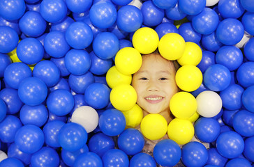 Smiling little girl playing with color plastic balls playground.