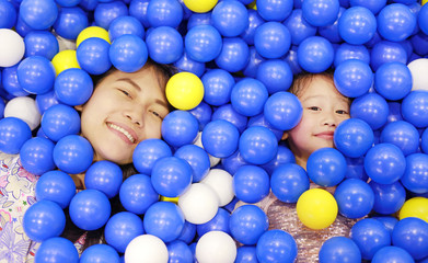 Happy mother and little girl playing with color plastic balls playground.