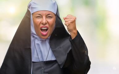 Middle age senior christian catholic nun woman over isolated background angry and mad raising fist...