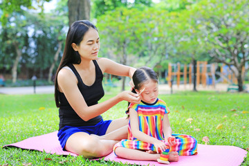 Mother combing daughter's hair lying in the green garden.