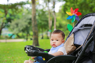 Close up Infant baby boy playing toy in hand sitting on stroller in nature park.