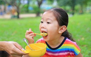 Close-up little asian child girl age about 4 years old eating rice by self in the garden outdoor.