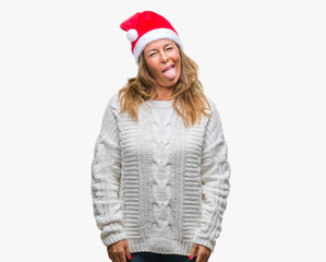 Middle age senior hispanic woman wearing christmas hat over isolated background sticking tongue out happy with funny expression. Emotion concept.