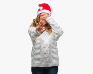 Middle age senior hispanic woman wearing christmas hat over isolated background covering eyes with hands and doing stop gesture with sad and fear expression. Embarrassed and negative concept.