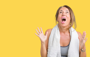Beautiful middle age woman wearing sport clothes and a towel over isolated background crazy and mad shouting and yelling with aggressive expression and arms raised. Frustration concept.