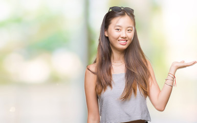 Young asian woman wearing sunglasses over isolated background smiling cheerful presenting and pointing with palm of hand looking at the camera.