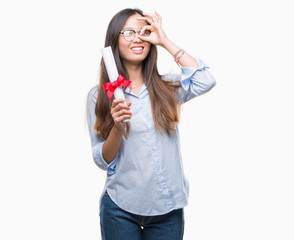 Young asian woman holding degree over isolated background with happy face smiling doing ok sign with hand on eye looking through fingers