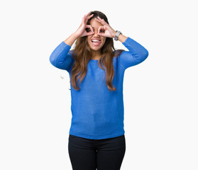 Young beautiful brunette woman wearing blue sweater over isolated background doing ok gesture like binoculars sticking tongue out, eyes looking through fingers. Crazy expression.