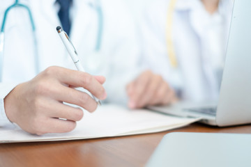 medical doctor in white uniform writing result and prescription on paperwork, medical concept