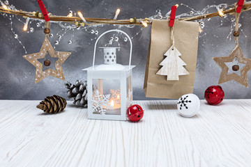winter decorations on white wooden table. burning candle lantern, paper present bags and wooden decorations against festive silver background