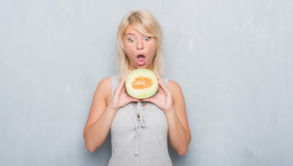 Adult caucasian woman over grunge grey wall eating cantaloupe melon scared in shock with a surprise face, afraid and excited with fear expression