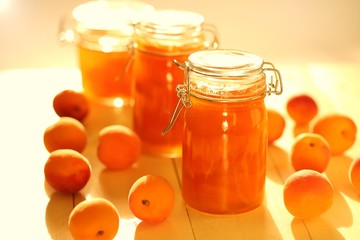 apricot jam set in glass jars and fresh ripe apricots on a yellow wooden board background in sun rays.Homemade jam