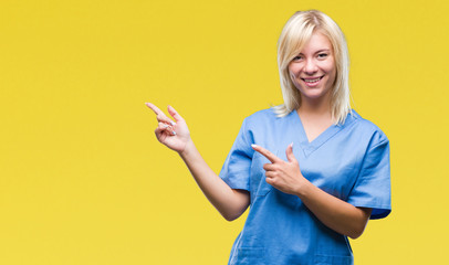 Young beautiful blonde nurse doctor woman over isolated background smiling and looking at the camera pointing with two hands and fingers to the side.