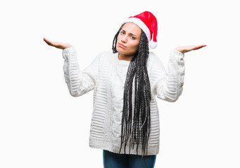 Obraz na płótnie Canvas Young braided hair african american girl wearing christmas hat over isolated background clueless and confused expression with arms and hands raised. Doubt concept.