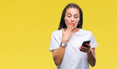 Young braided hair african american girl showing using smartphone over isolated background cover mouth with hand shocked with shame for mistake, expression of fear, scared in silence, secret concept