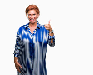 Atrractive senior caucasian redhead woman over isolated background doing happy thumbs up gesture with hand. Approving expression looking at the camera with showing success.