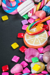 different sweets, candies, lollipops and chewing gum on black background