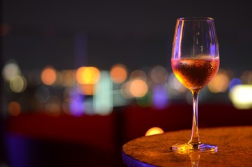A glass of Rosé wine with bokeh light at Bangkok city and colorful light from rooftop building.