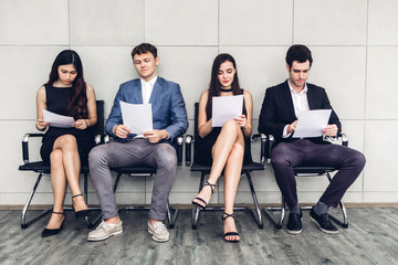 Group of business people holding paper while sitting on chair waiting for job interview against wall background