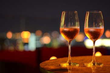 Two glasses of Rosé wine with bokeh light at Bangkok city and colorful light from rooftop building.