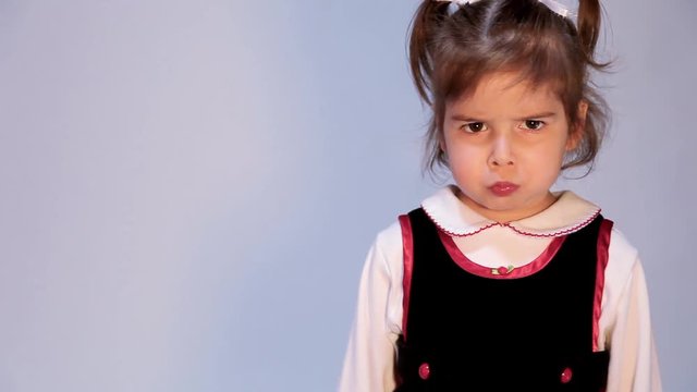 Adorable, expressive little girl talks to the camera and goes into a grumpy, pouty face with lower lip stuck out and eyebrows furrowed and down.  She scrunches her nose.  There is copy space.