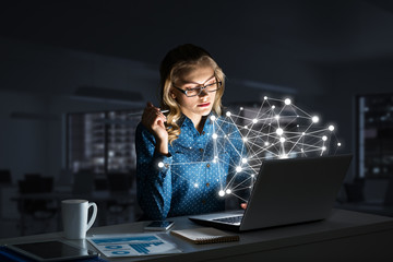 Attractive blonde wearing glasses in dark office using laptop. Mixed media