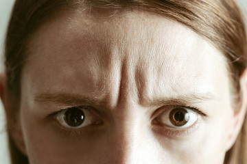 Fototapeta premium Młoda kobieta z wyrazem twarzy, widoczne zmarszczki na czole, strzał studio zbliżenie